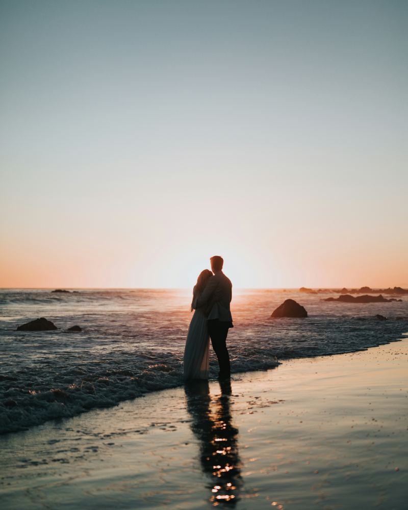 Couple qui s'étreint sur une plage devant un coucher de soleil