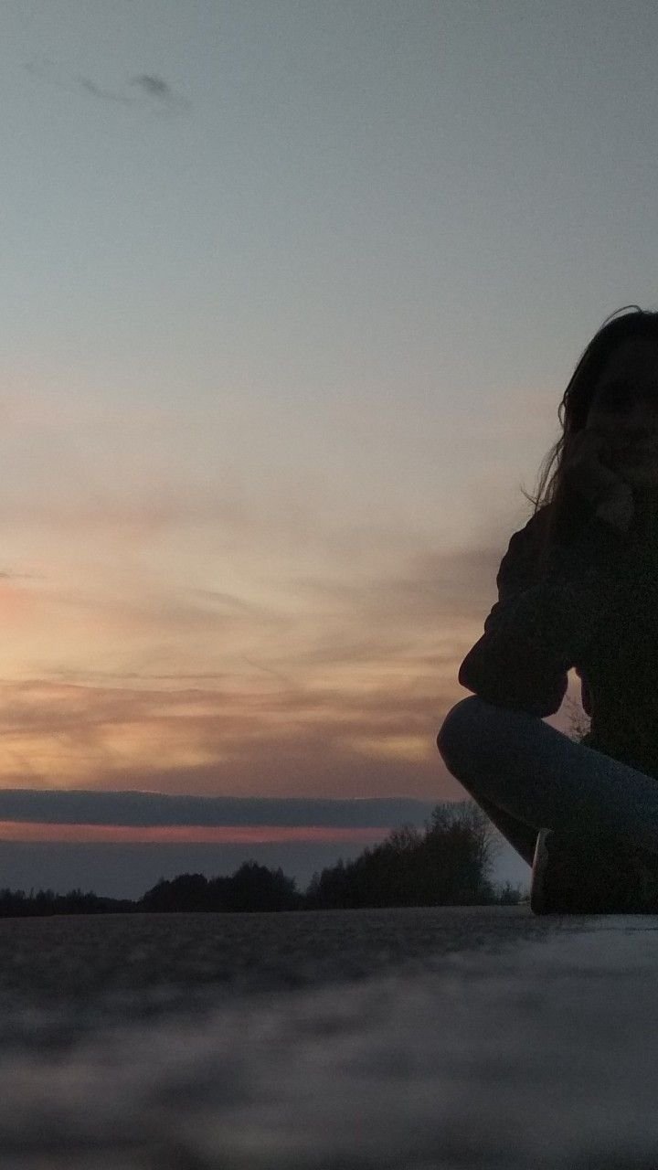 Adolescente assise au sol en silhouette, le visage dans les mains, face à un coucher de soleil