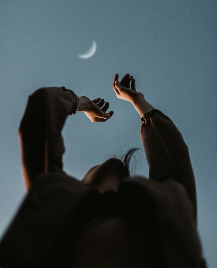 Vue en contre-plongée des mains d'une adolescente tendues vers un croissant de Lune dans le ciel