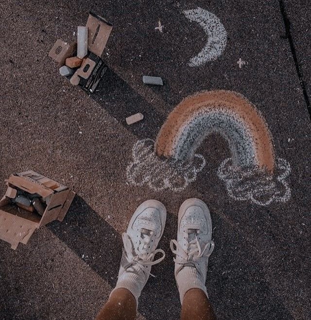 "Dessin à la craie d'un croissant de Lune et d'un arc-en-ciel sur le sol, aux pieds d'un adolescent en baskets