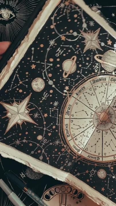 Page de carnet noire où sont dessinés à l’encre dorée la roue du zodiaque et les constellations