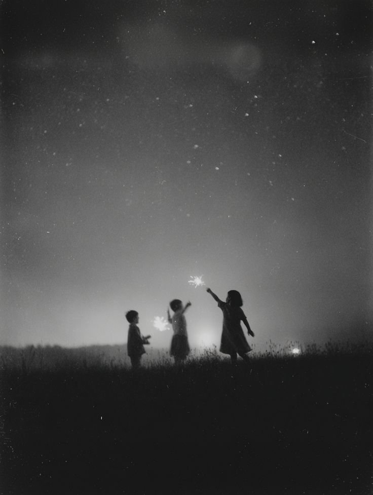 Trois enfants en silhouette jouant avec des cierges magiques sous un ciel étoilé, en noir et blanc