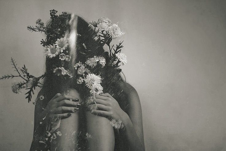femme en noir et blanc assise avec les genoux contre son torse visage caché par un bouquet de fleurs