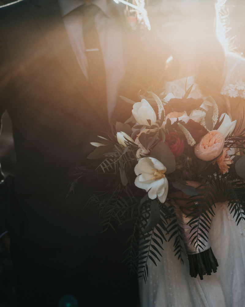 Couple de mariés à contre jour, la mariée porte un gros bouquet