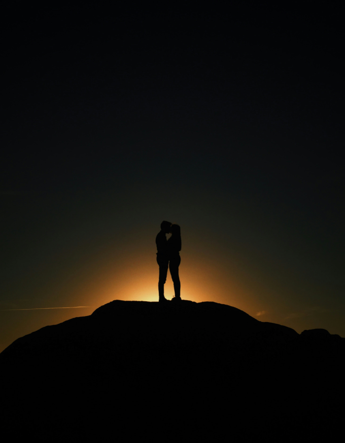 Silhouettes d'un couple qui s'étreint et s'embrasse en haut d'une colline avec un coucher de soleil en arrière plan