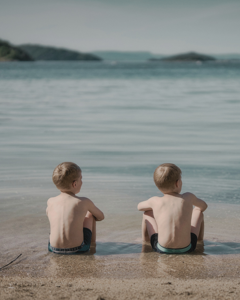 Jumeaux de dos assis dans l'eau sur une plage