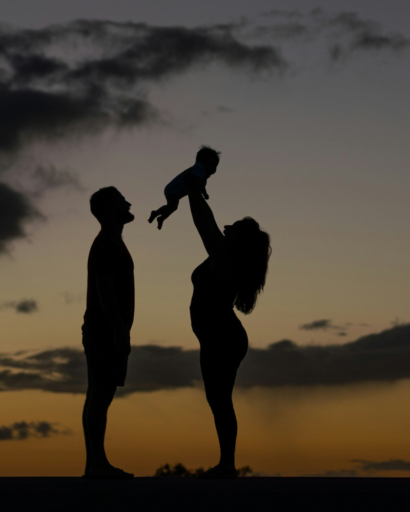 Des parents avec leur enfant dans les bras à contre-jour