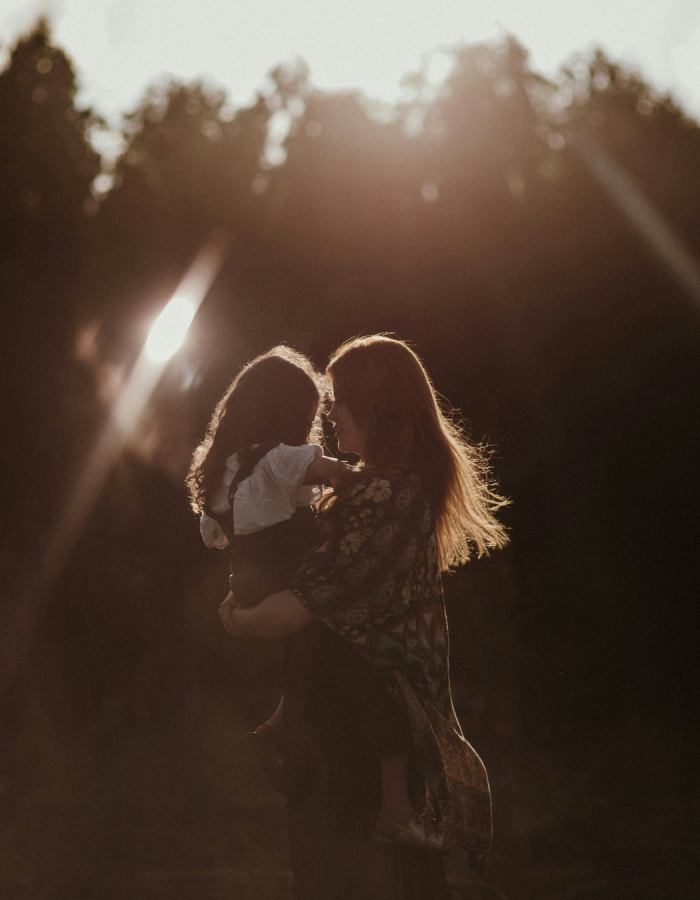 Mère qui tient sa fille dan les bras à contrejour éclairées par les rayons du soleil
