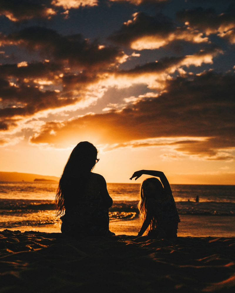 Photo à contre-jour d'une mère et sa fille assise au bord de mer