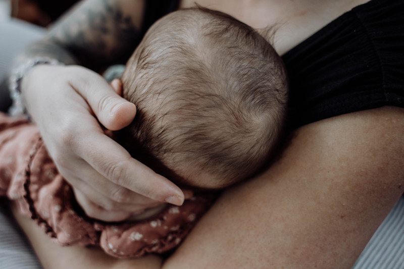Alt="Photographie des bras d'Anaïs fondatrice de Celeste Ceremonia portant son bébé, la main posée à l'arrière de sa tête que l'on aperçoit de dos pour illustrer un article du blog"